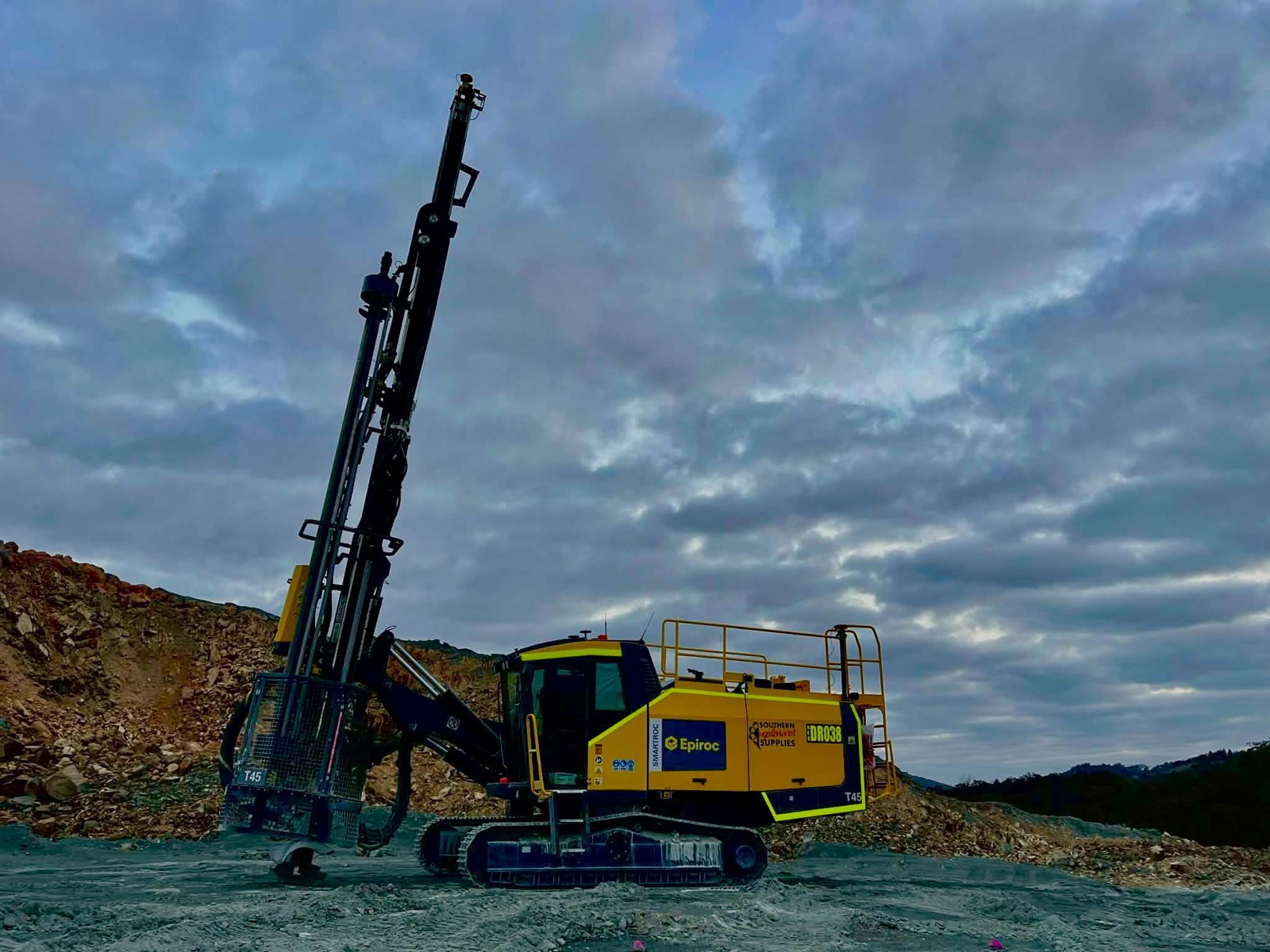 Yellow drill rig on a bench under storm clouds