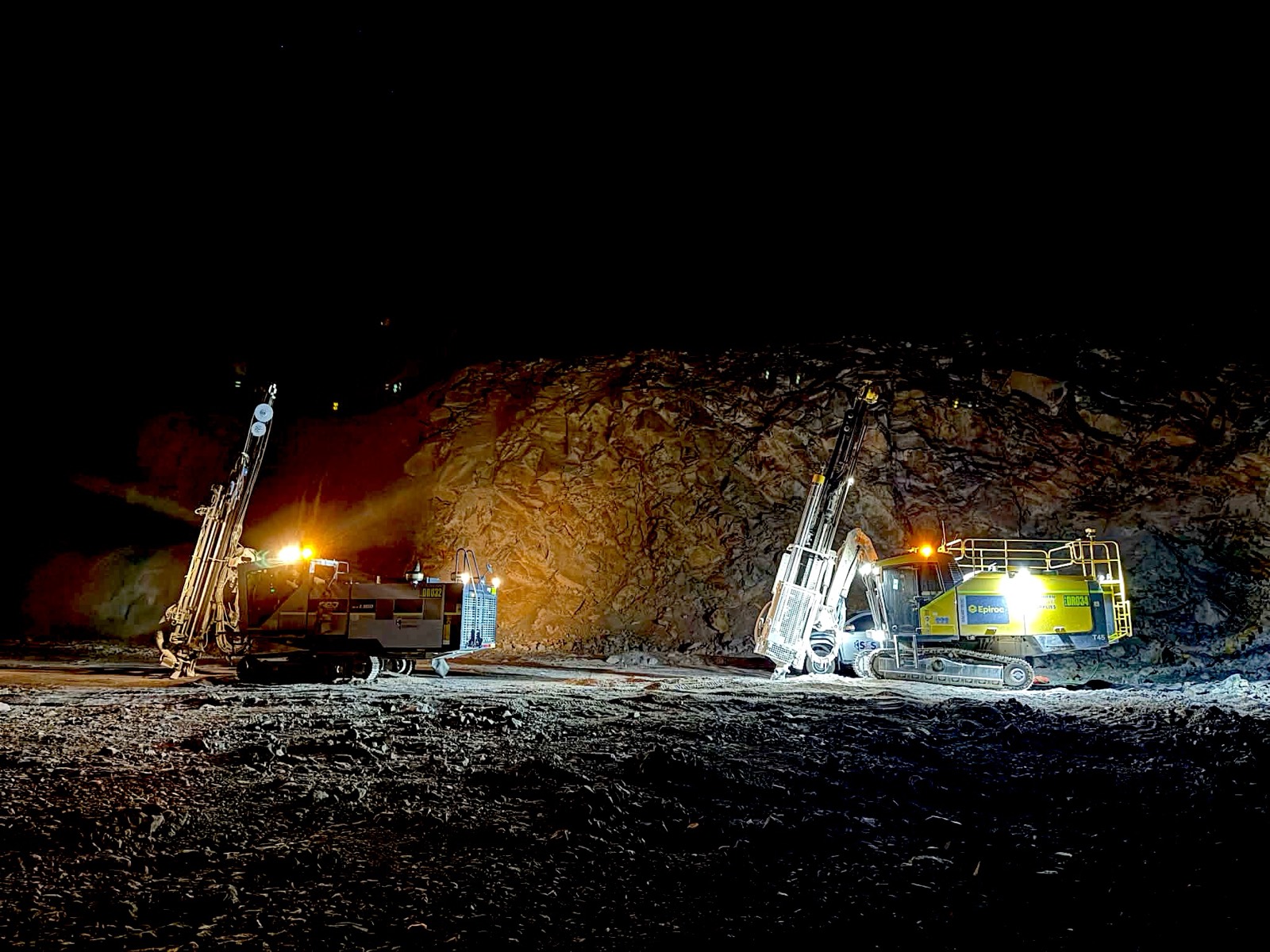 Yellow Epiroc drill rigs working under lights on night shift
